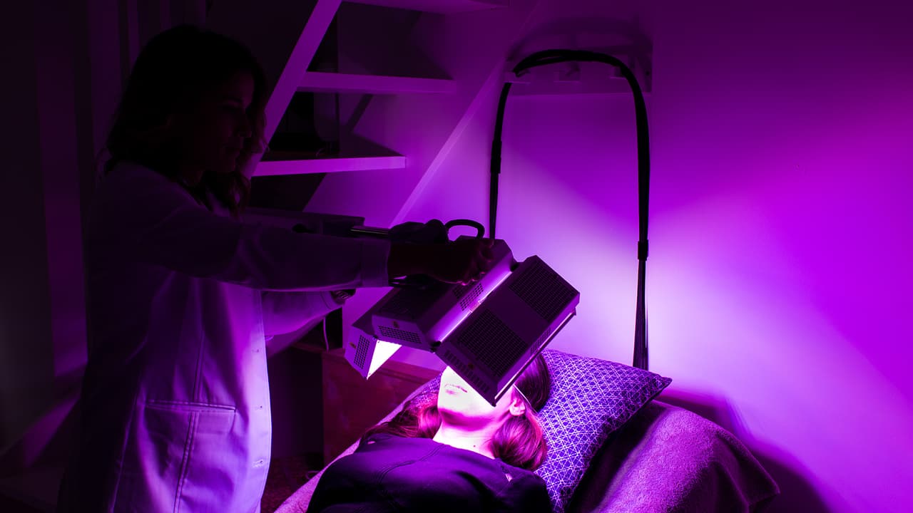 Le Docteur Emma Lavocat positionne l'appareil de traitement par LED sur le visage d'une patiente.